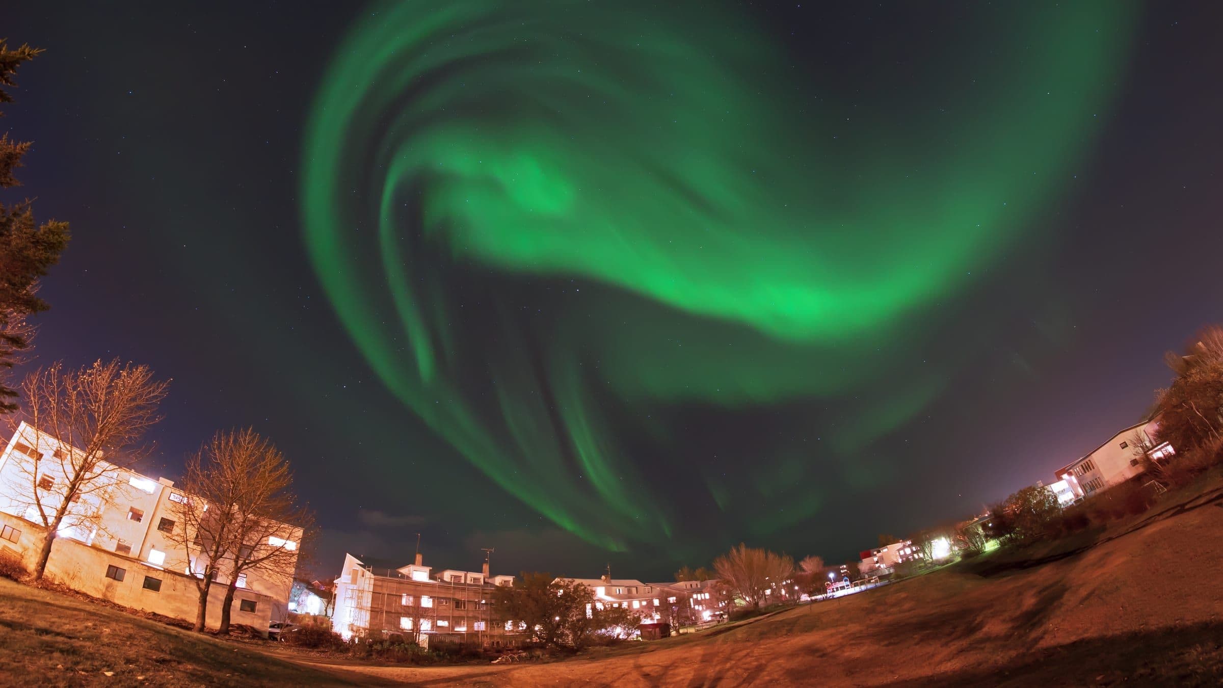 Espiral de aurora boreal girando sobre las casas iluminadas de un barrio residencial de Reikiavik.